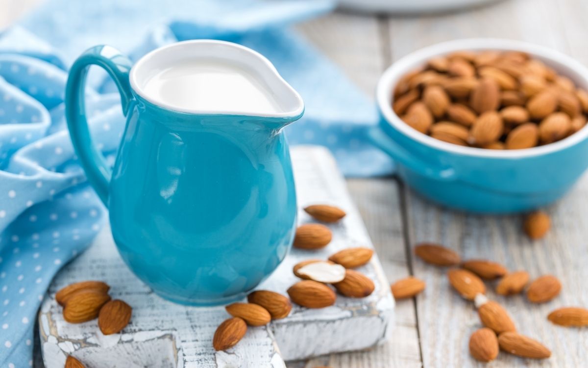 A bowl of almonds next to a carafe of almond milk.