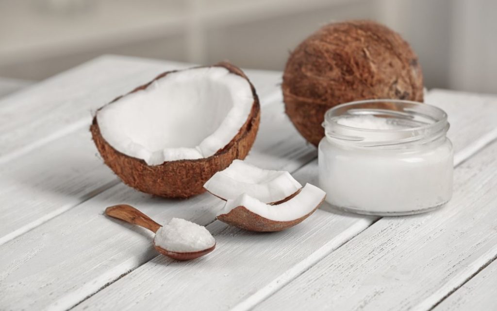 Coconut oil in a jar sits next to an open coconut.