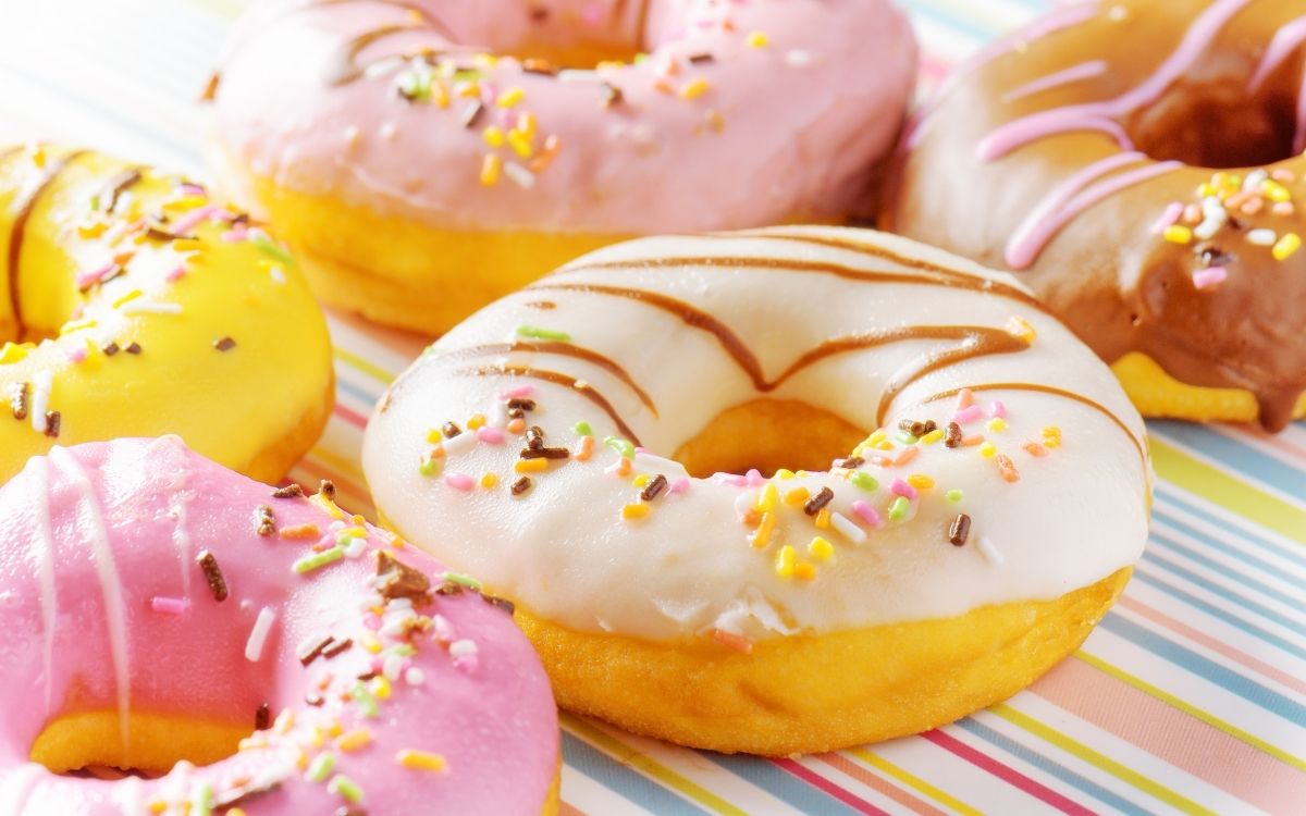 Delicious looking colorful donuts sit on a colorful pinstripe tablecloth.