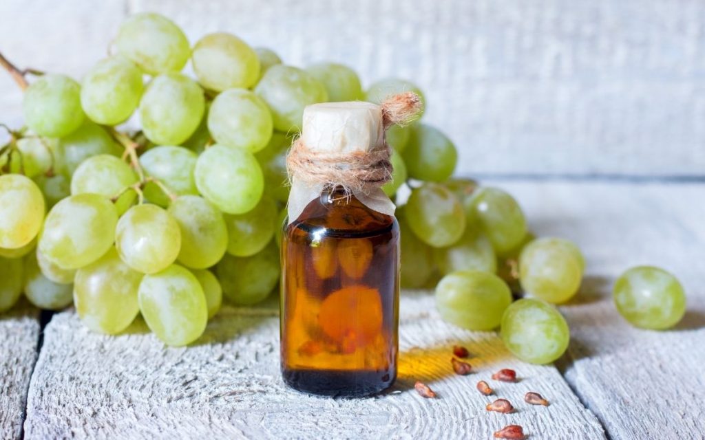 Grapeseed oil sits in front of a bunch of grapes.