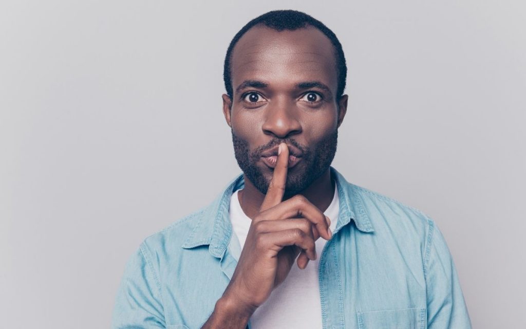 Man is holding his finger over his lips implying to stay quiet. 