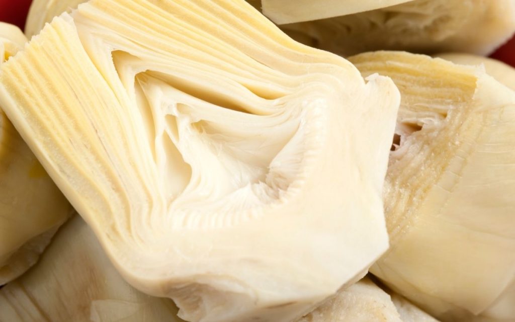 Sliced artichoke heart atop a pile of sliced artichoke hearts.
