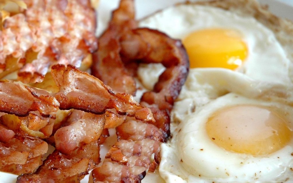 Sizzling bacon on a plate with eggs.