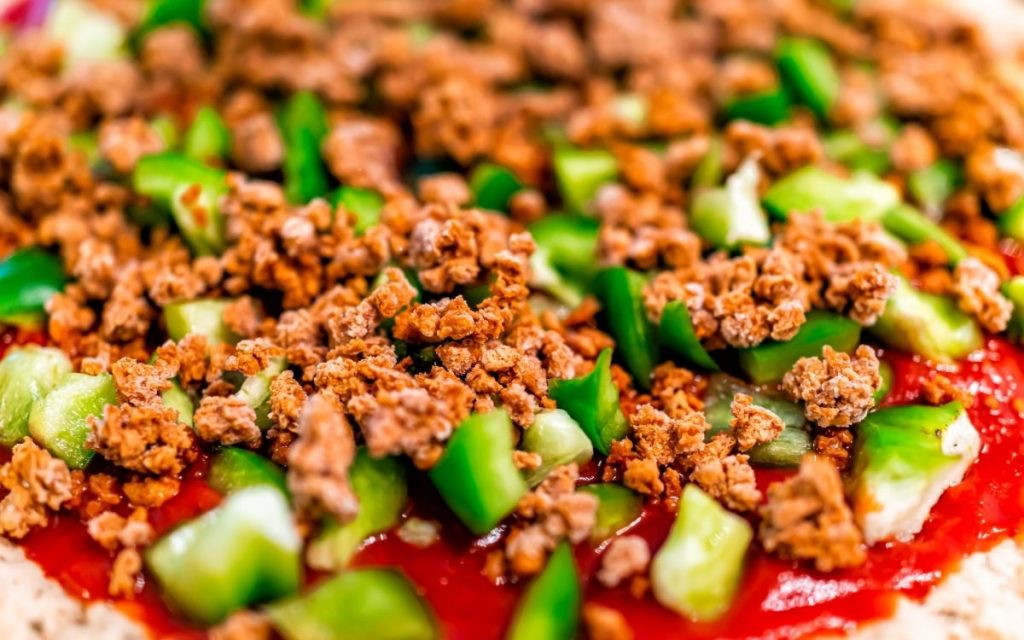 Beef crumbles atop an uncooked pizza.