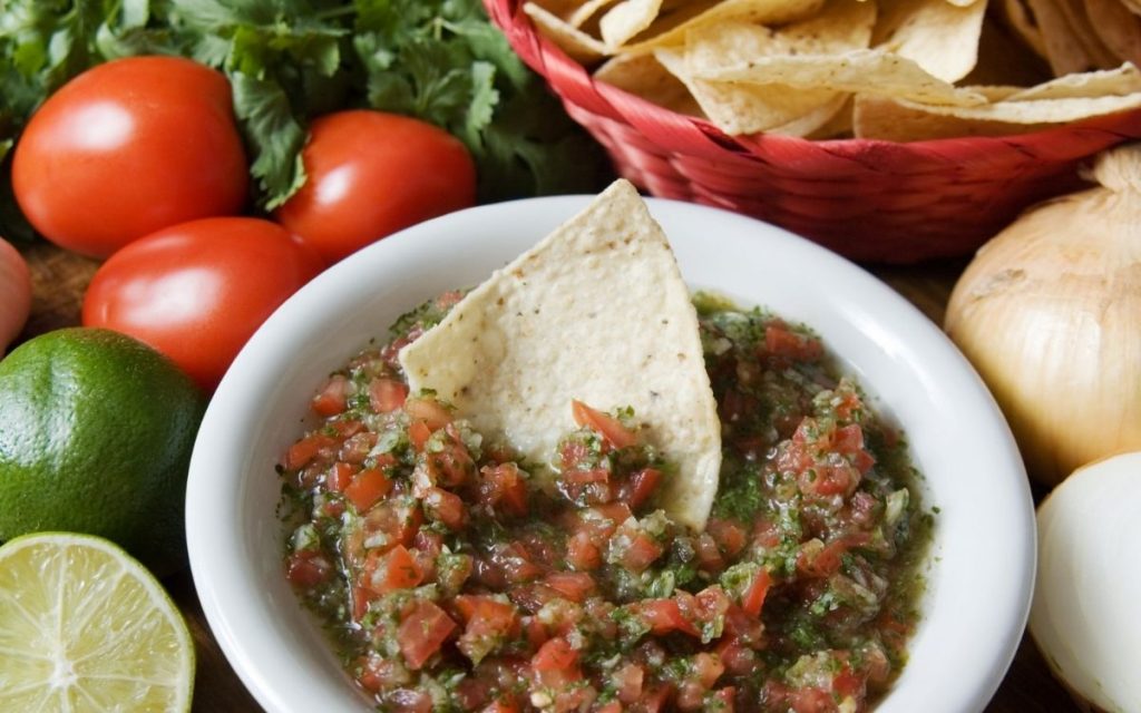 A bowl of salsa with a chip being dipped.