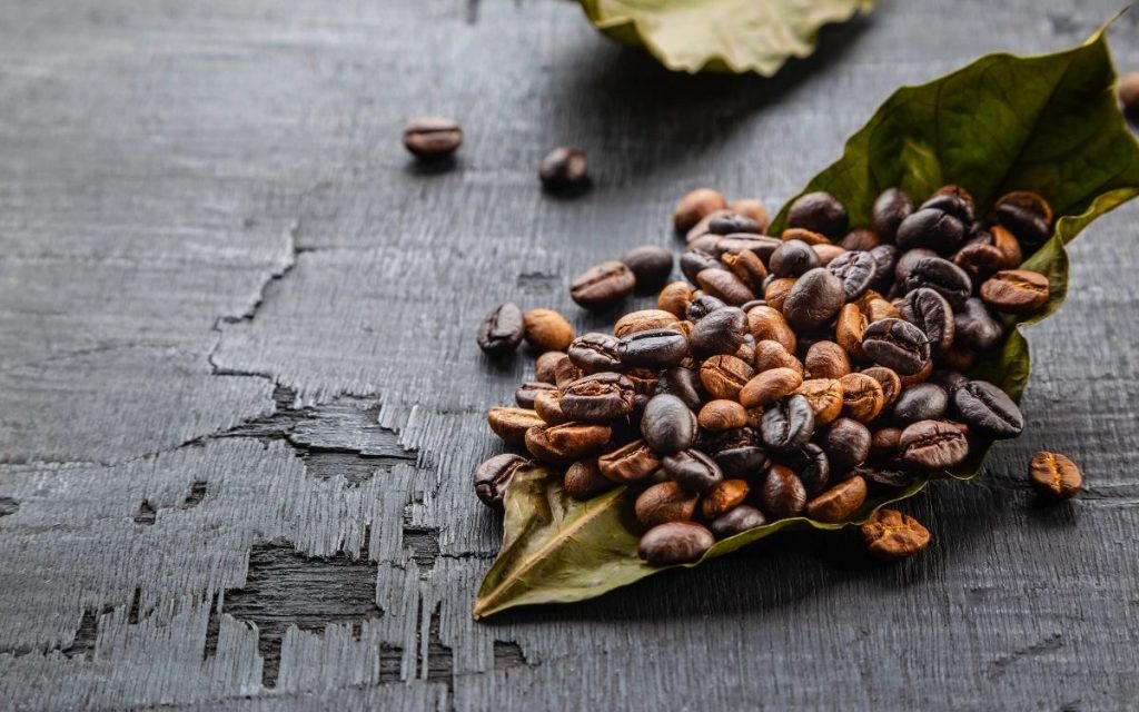 Coffee beans cover a leaf on a table.
