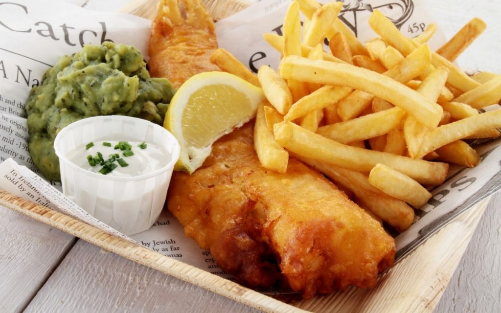 A basket with fish and chips with lemon wedge and tartar sauce.