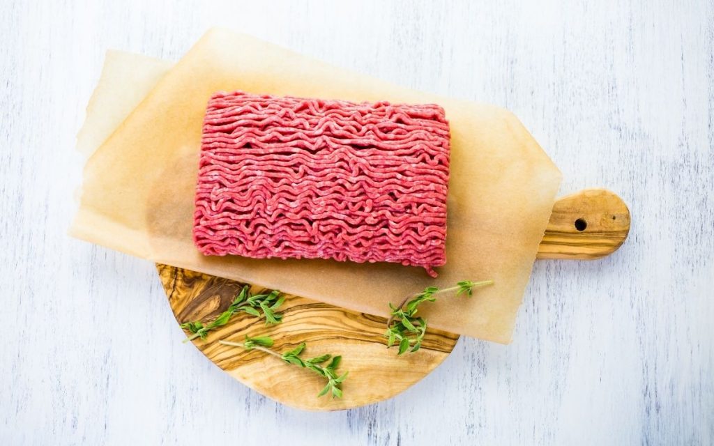 A slab of ground beef sits on top of a cutting board.