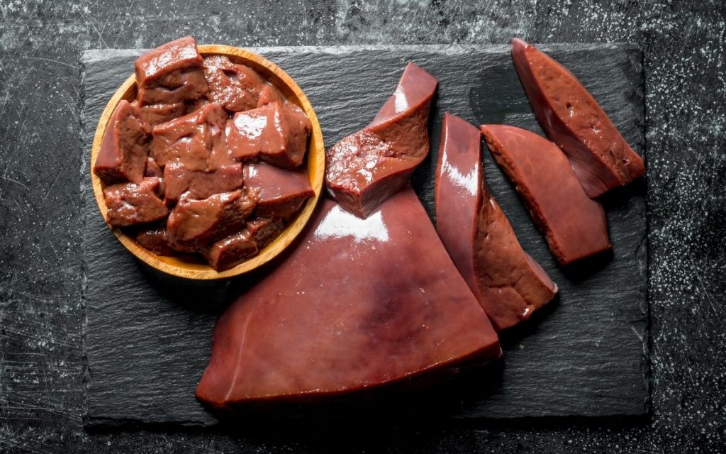 Slices of liver lay flat on a cutting board with a bowl of liver chunks next to it.