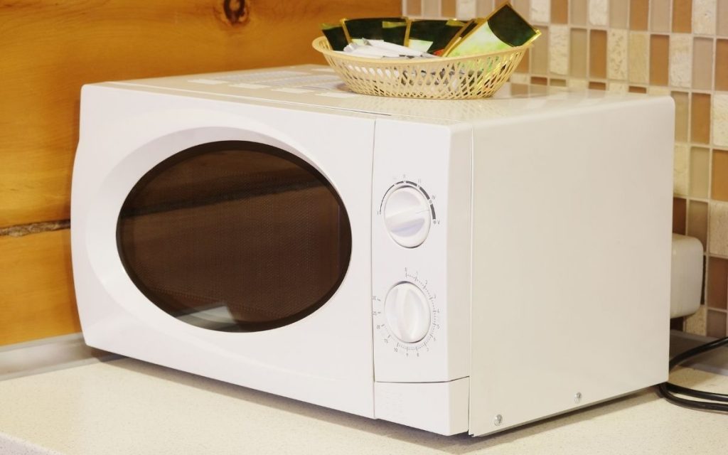 An older looking model of a microwave with an oval shaped window sits on a table.