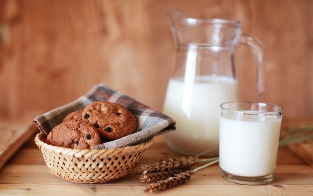 A basket of cookies sit next to a glass and pitcher of milk.