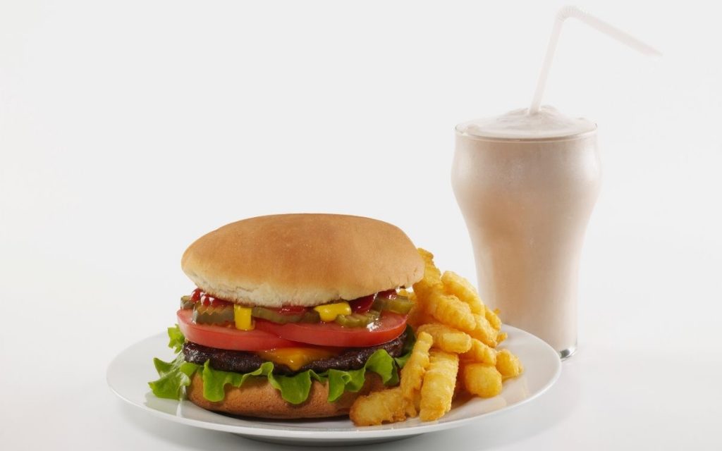 A burger & fries on a plate sitting next to a milkshake.