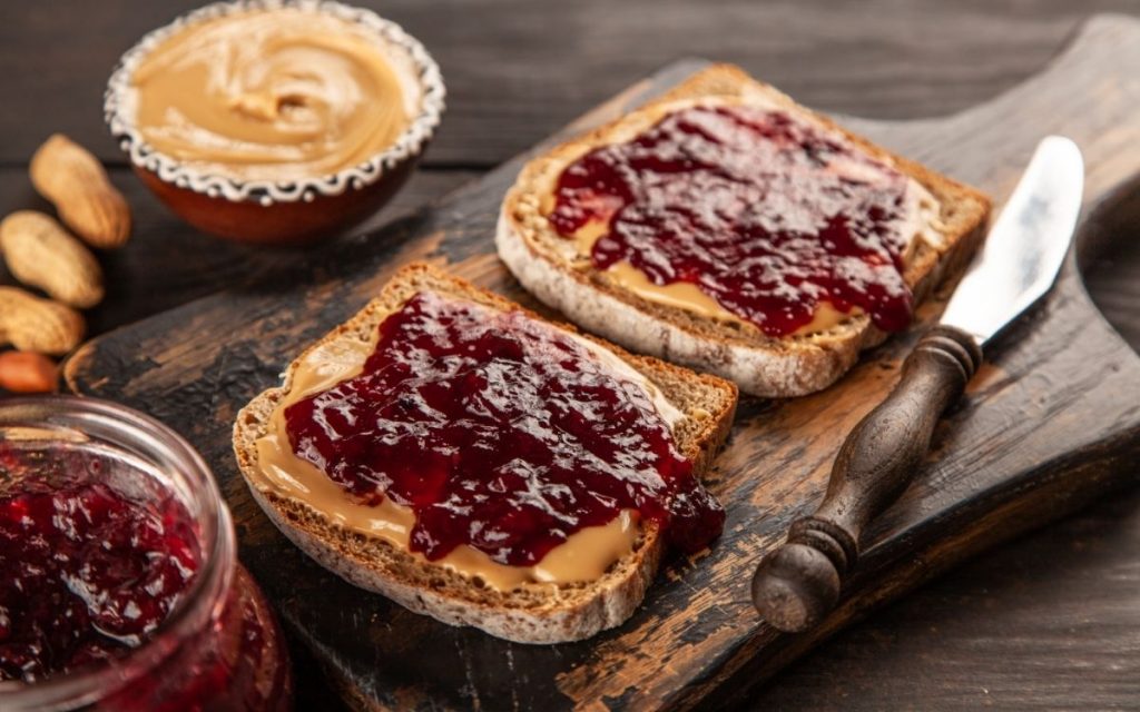 Peanut butter and jelly freshly spread on top of two pieces of bread.