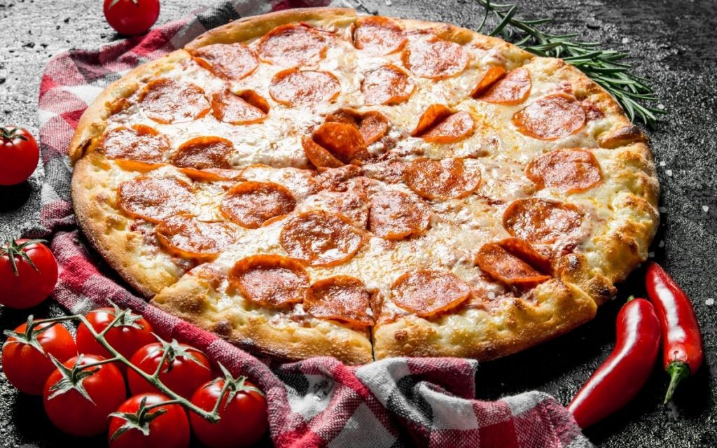 Pepperoni pizza on a table next to fresh tomatoes on the vine.