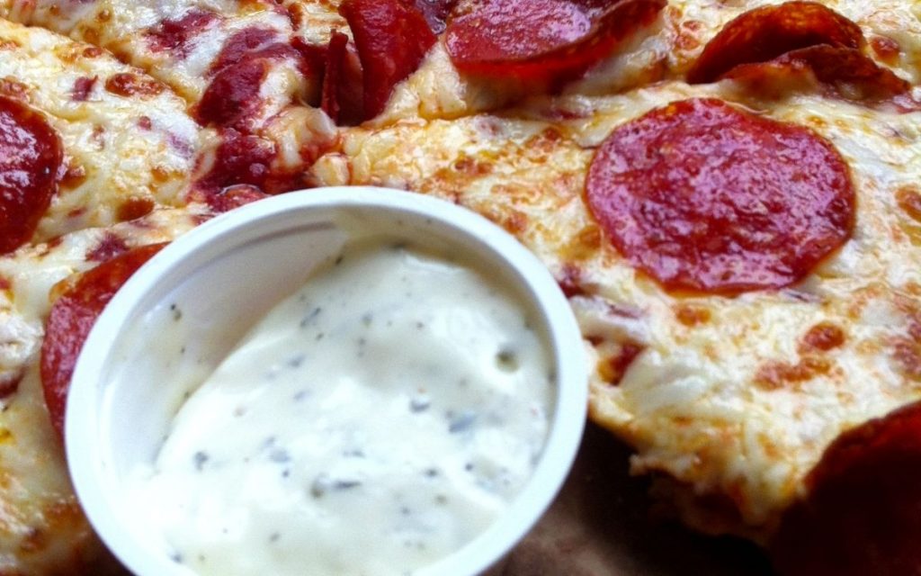 Pizza sitting next to a plastic cup of ranch.