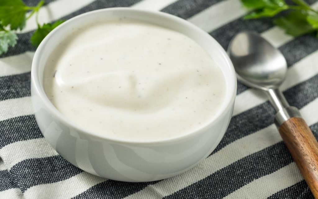 Creamy homemade ranch dressing in a bowl on a striped tablecloth.