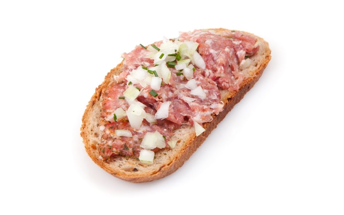 Raw ground beef and onions spread on top a piece of bread.