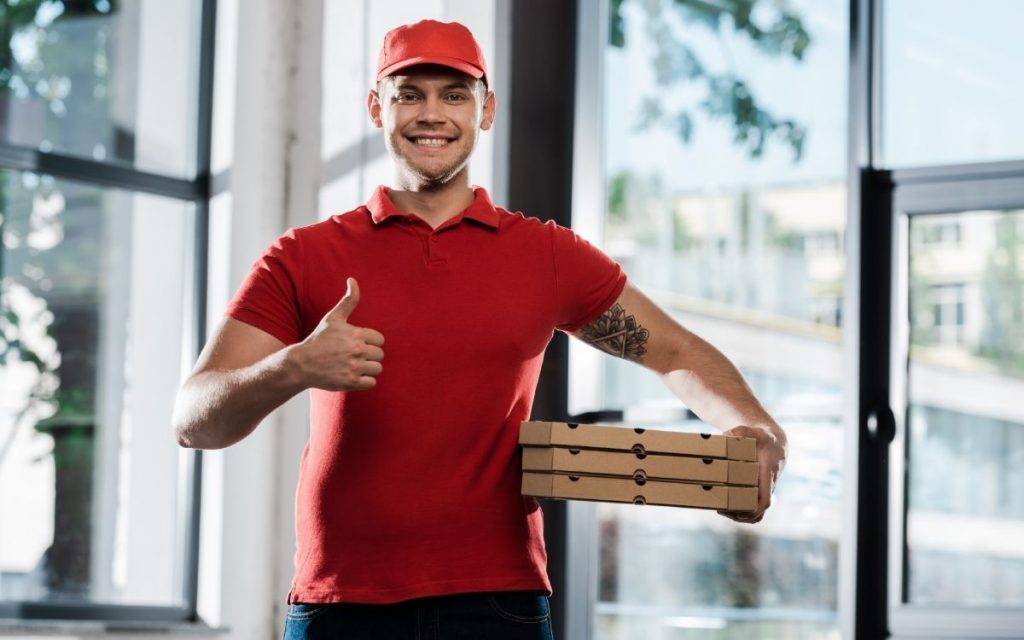 Man with pizza boxes looks happy and holds his thumb up.