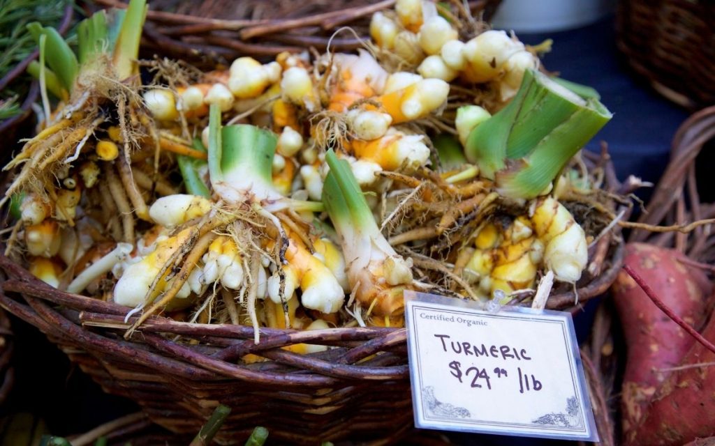 Turmeric root in a basket with a sale sign at a farmers market.