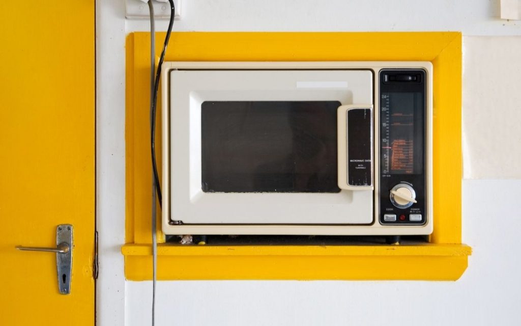 A retro looking microwave sits in a wall in a house.