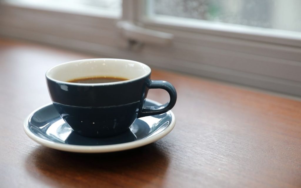 A cup of coffee on a table with a window in the distance.