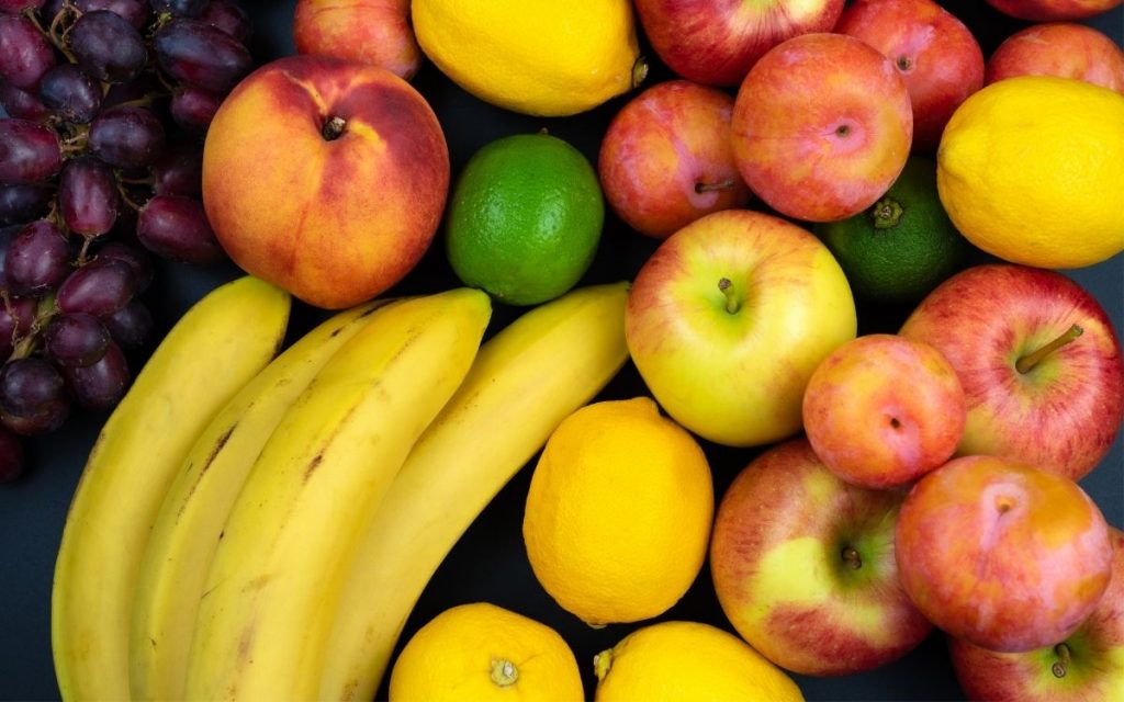 Various fruits like banana, apple, and lemon sit on a table.