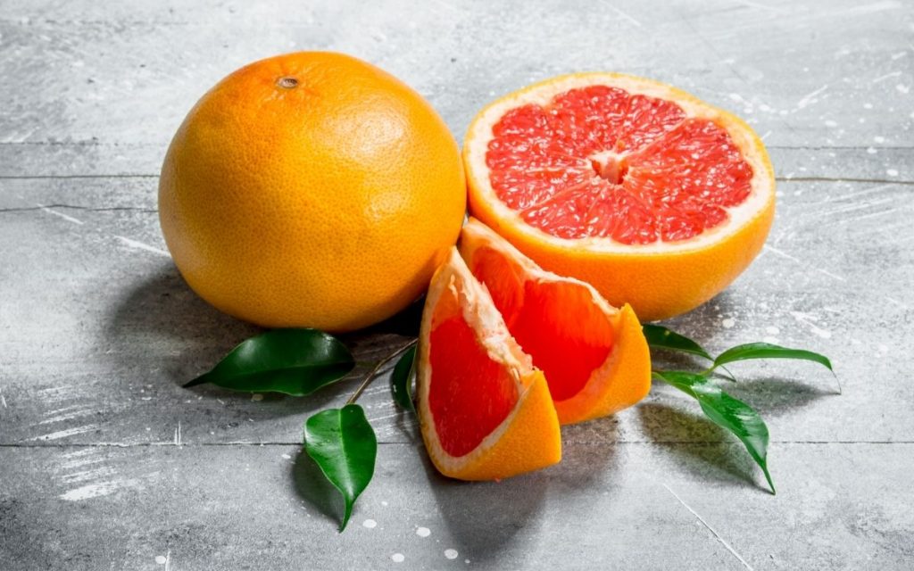A whole grapefruit next to a sliced grapefruit.