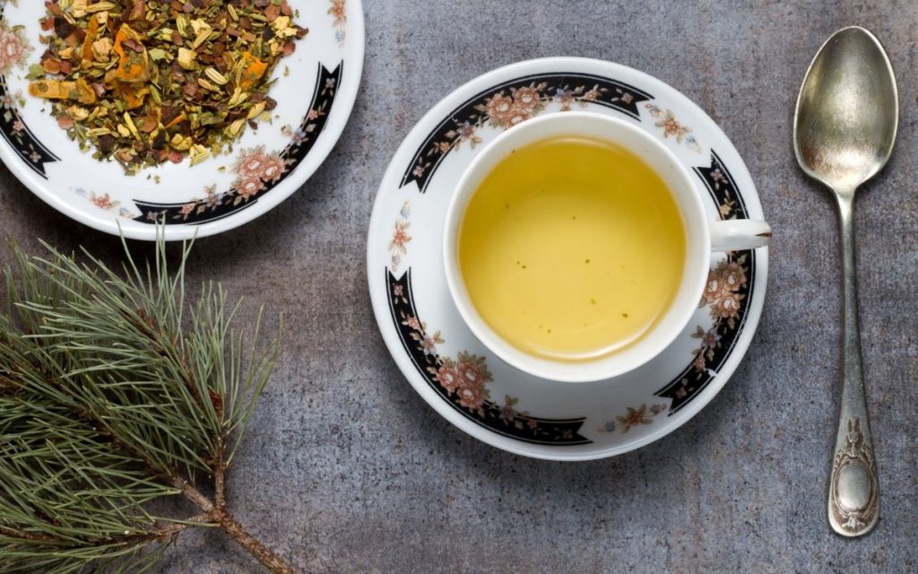 A cup of green tea next to green tea herbs.