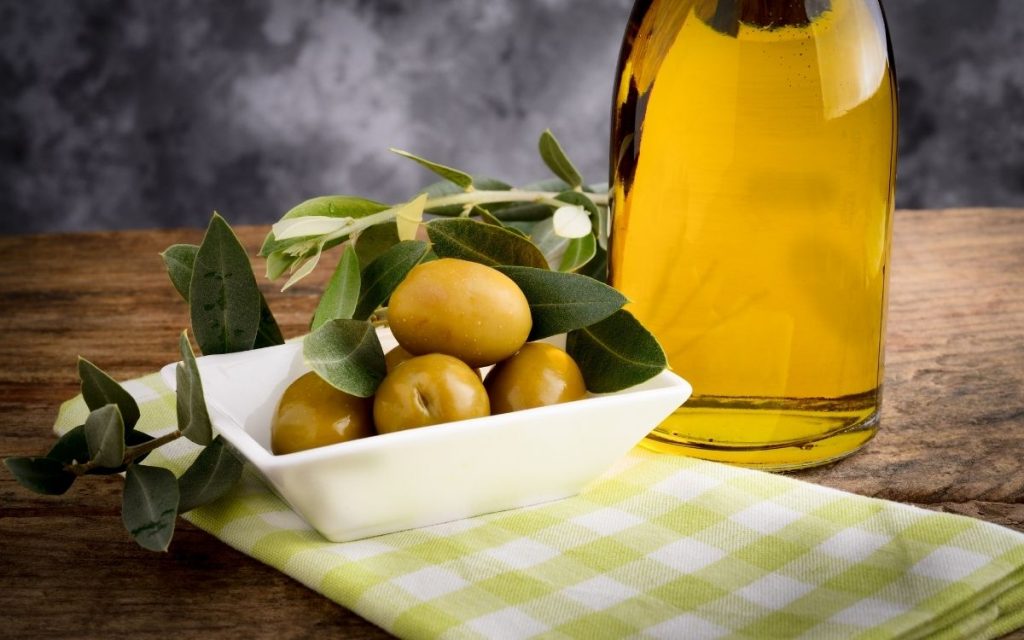 A small dish with olives next to a bottle of olive oil.
