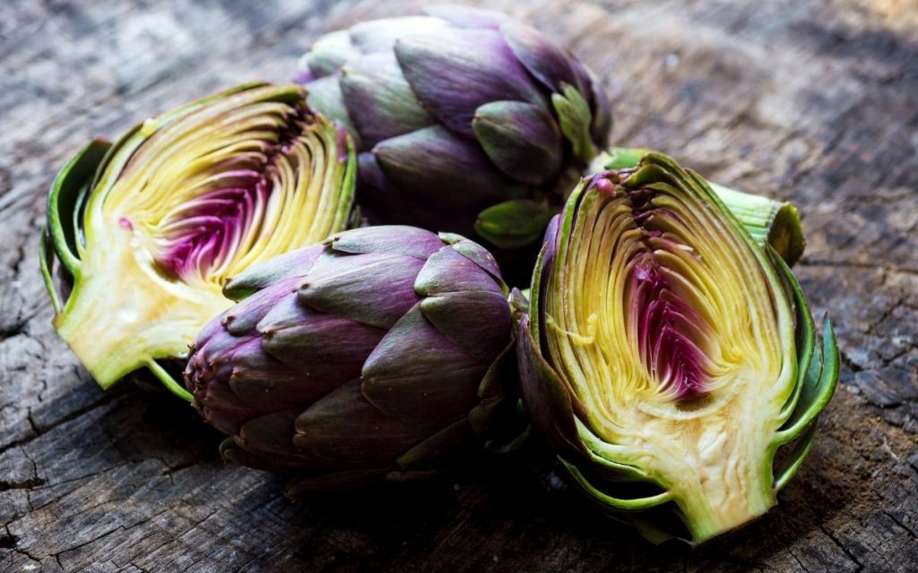 halved and whole fresh artichokes on rustic cutting board